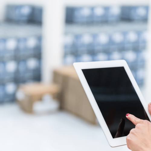 Person using a tablet for inventory management in a commercial cleaning context, with storage boxes in the background.