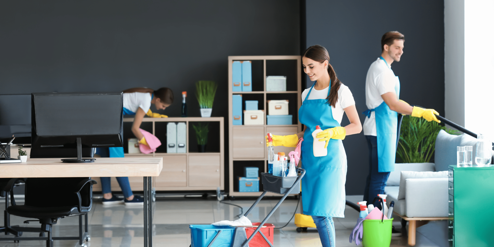 Commercial cleaning team in office setting, featuring workers in blue aprons and yellow gloves using cleaning supplies and equipment, emphasizing professional cleaning services.