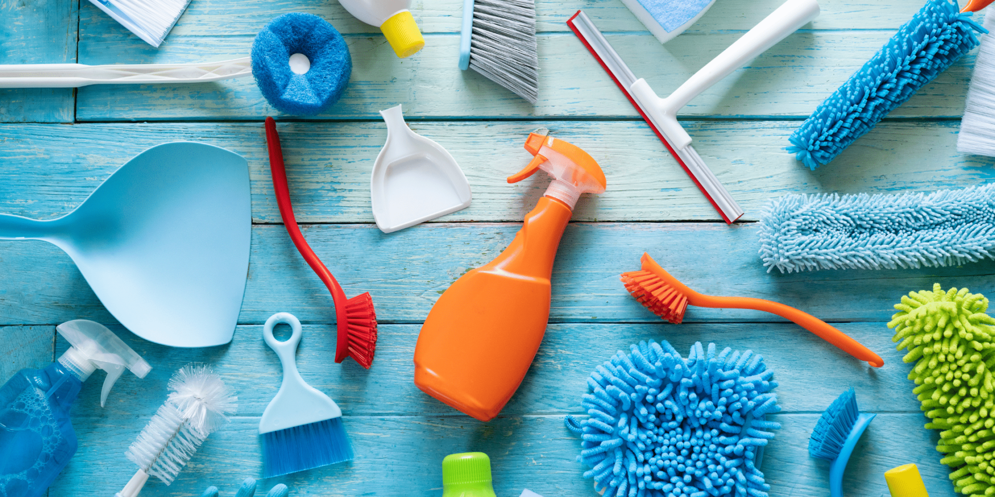 Colorful array of cleaning supplies, including spray bottles, brushes, sponges, and dustpans, arranged on a blue wooden surface, symbolizing Clean Corps' comprehensive cleaning services for residential and commercial needs.