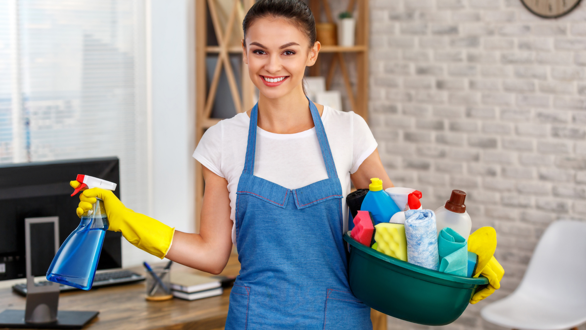 Smiling woman in blue apron holding cleaning supplies and spray bottle, representing professional cleaning services for homes and offices.
