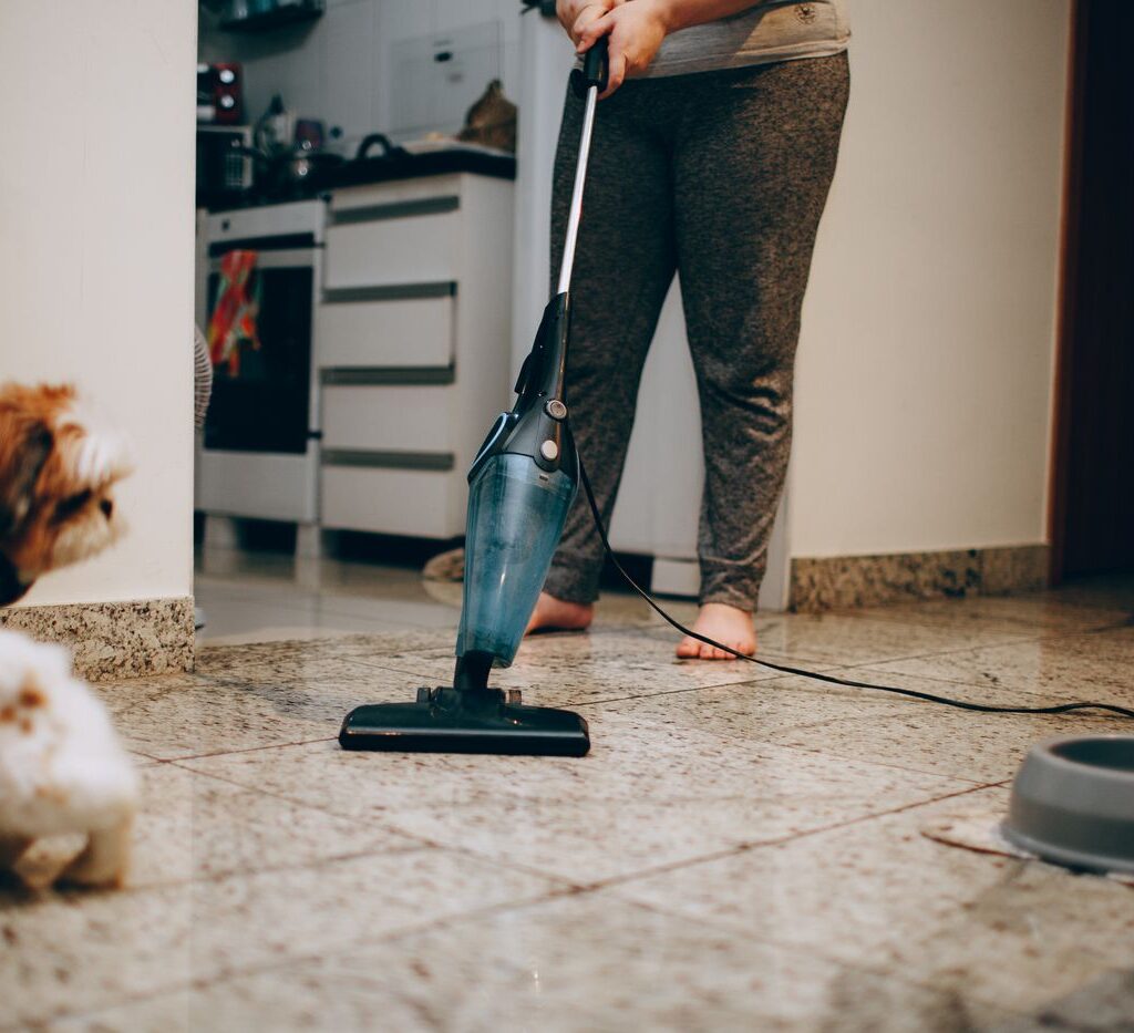 Vacuuming a tile floor at home while pets look on, part of a weekly household cleaning schedule in Orlando
