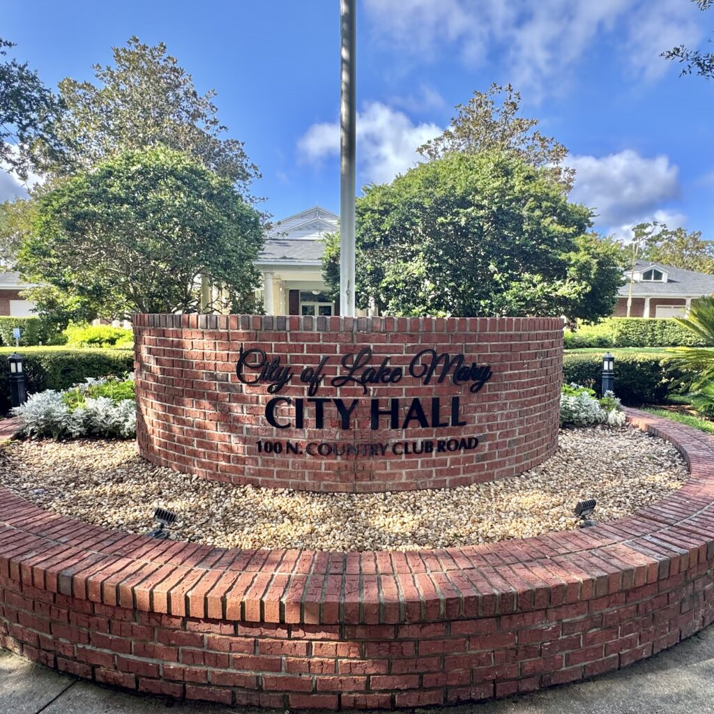 Curved red-brick sign reading City of Lake Mary City Hall in front of the white-columned city hall building, Lake Mary, Florida