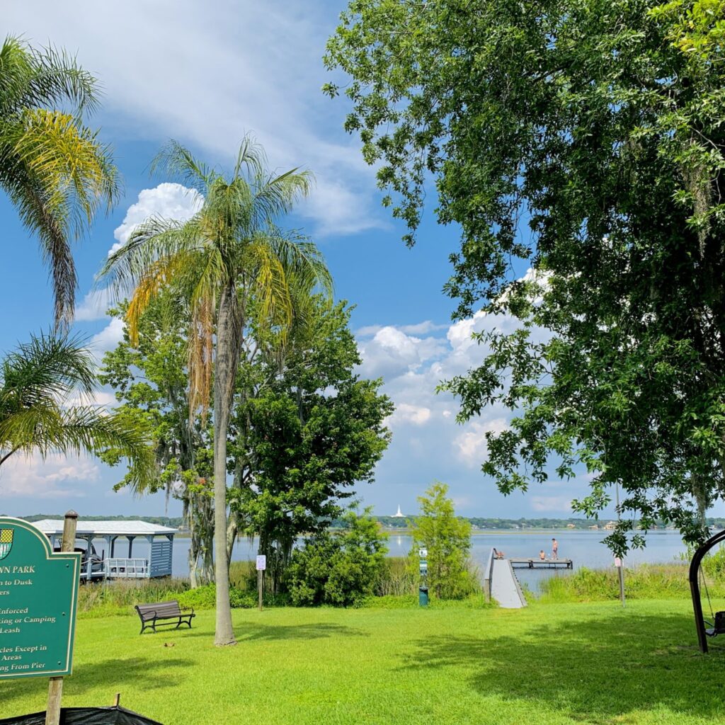 Lake Down Park in Windermere, Florida, with lawn, palms and oaks leading to a dock on the lake under a blue sky